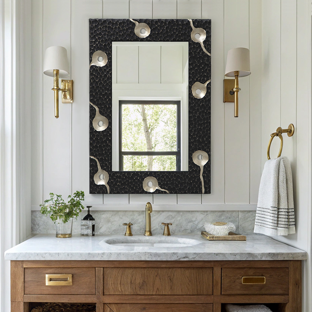 Carved framed mirror installed in a modern bathroom, featuring marble countertop, brass fixtures, and wall sconces.